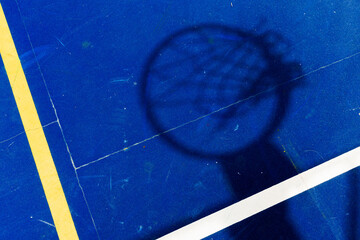 Shadow of a basketball hoop cast on a vivid blue court with yellow and white lines, viewed from...