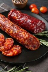 Cut smoked sausages, rosemary and tomatoes on black table, closeup
