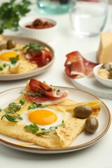 Delicious crepes with eggs and bacon served on white table, closeup