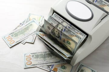 Money counter machine with dollar banknotes on white wooden table, above view