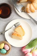Pieces of delicious bundt cake, Easter eggs, tulips and tea on gray table, flat lay