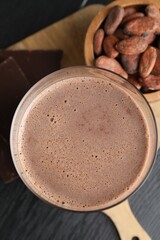 Tasty chocolate milk, bars and cocoa beans on black wooden table, top view