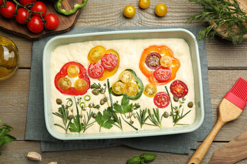 Raw focaccia with vegetables, spices and brush on wooden table, flat lay