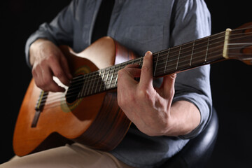 Fototapeta premium Man playing guitar on black background, focus on hand