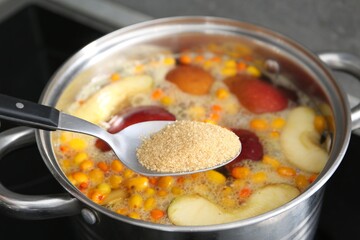 Adding sugar into tasty compot in pot on stove, closeup