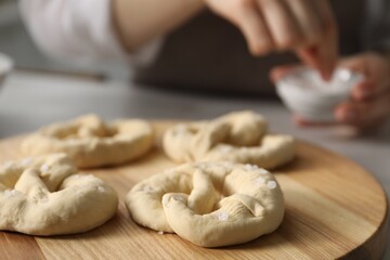 Woman adding sea salt onto uncooked pretzels at table indoors, selective focus
