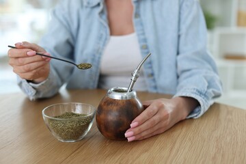 Woman making traditional yerba mate tea at wooden table indoors, closeup