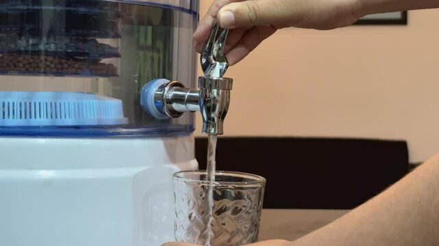 Ni&ntilde;o llenando vaso de agua de un purificador o filtro.