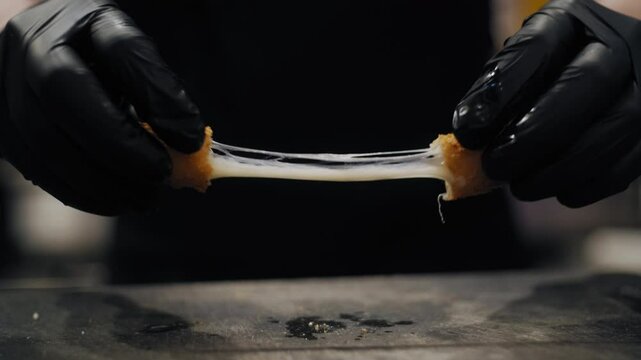 A chef in black gloves breaks open a freshly fried cheese stick, revealing hot, melted cheese stretching between the halves.