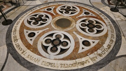 Florence, Italy - 3 January 2025. Marble tomb of Saint Zenobius in the Florence Duomo floor, marked by circular inlays, Latin inscription, and a central bronze grate.