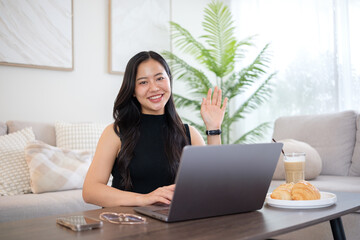 Young woman using laptop in the living room with coffee and croissant, enjoying a relaxed  morning.