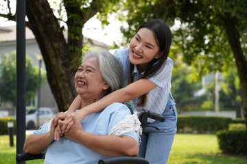 Naklejka premium Two women, the daughter pushing a stroller with her elderly mother, walk in the garden and chat happily.