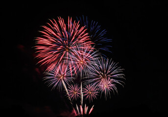 Colorful fireworks lighting up the night sky above a crowded cityscape, reflecting in a serene river below, creating a breathtaking spectacle.
