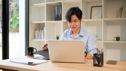 Smiling young business man analyzing paperwork and managing financial data in a office.