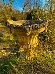  Weathered yellow stone garden pot in lush english countryside setting