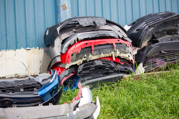 A pile of various used car bumpers stacked outdoors near a metal wall, showing automotive waste and recycling potential
