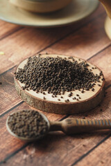 Black tea leaves displayed on wood with spoon and cup in background