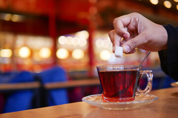 Hand stirring sugar into a cup of tea in a cozy cafe setting