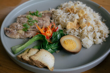 A plate of hainan chicken rice served with bok choy, egg and other vegetable toppings in a restaurant