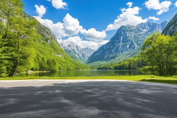 Naklejka premium Scenic alpine lake nestled in a valley, surrounded by lush greenery and towering mountains under a vibrant blue sky. Empty asphalt road leads to the tranquil scene