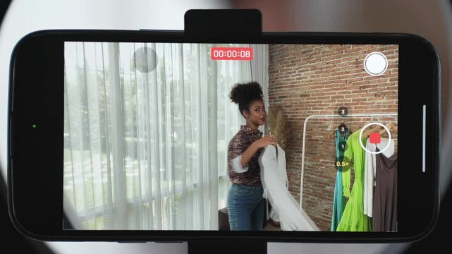 Rear view behide smartphone screen recording woman influencer shoot live stream vlog video review clothe crucial social media or blog. Girl with apparel studio lighting for marketing broadcast online