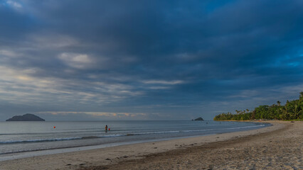 Tropical sandy beach. Silhouettes of people in the turquoise ocean. The waves are quietly foaming....