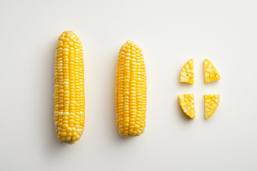 A two whole sweet corn cob alongside a few neatly cut pieces, isolated on a bright white background.
