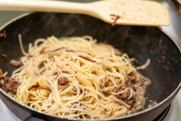 Thin spaghetti with tender chunks of stewed beef is being heated in a skillet on an electric stove, showcasing a delicious and hearty meal preparation