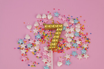 Gold birthday candle and sprinkles on pink background. Number 7.	