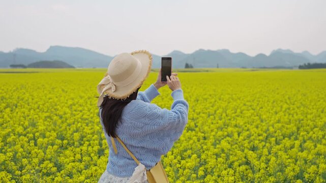 Young happy woman tourist taking photo and enjoying the canola fields while traveling in Luoping, China