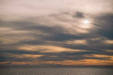 Fototapeta premium Blue water stretches to the horizon where sea and sky meet, clouds drifting gently as sunlight dances on the ocean, creating a breathtaking natural landscape.