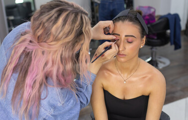 Woman is sitting in a chair while another makeup artist is applying makeup to her face. The woman...