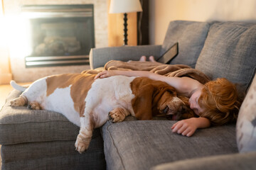 Boy and large basset hound pet lay together under blanket on couch
