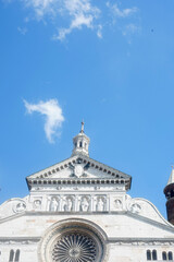 Crema Cathedral facade featuring statues of saints and a grand rose window rises against a vibrant blue sky with scattered clouds