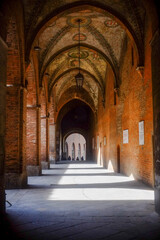 Sunlight streaming through historic hallway, highlighting brick walls and frescoed vaults of Palazzo de Comune in Cremona