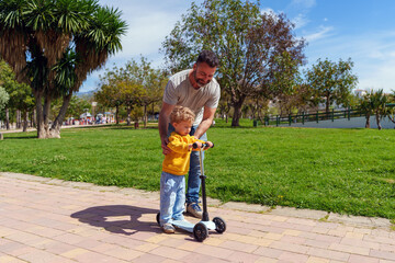 Parent teaching child scooter skills, sharing bonding moment during outdoor learning experience in sunlit park setting