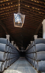 Obraz premium Interior of a traditional winery with rows of stacked wooden barrels creating a hallway and a vaulted wooden ceiling.