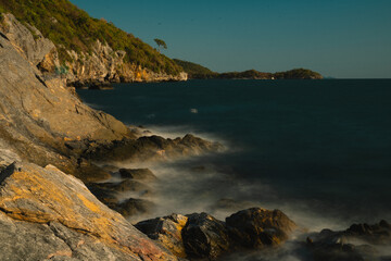 Fototapeta premium As the sun set over the ocean, waves crashed against the rock-strewn beach, painting a golden seascape and revealing a breathtaking landscape shaped by nature and sea.