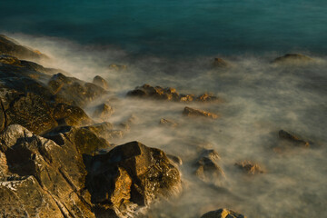 As the sun set over the ocean, waves crashed against the rock-strewn beach, painting a golden seascape and revealing a breathtaking landscape shaped by nature and sea.