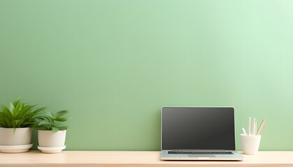 Minimalist workspace with laptop, green plants, and stationery on wooden desk against green wall