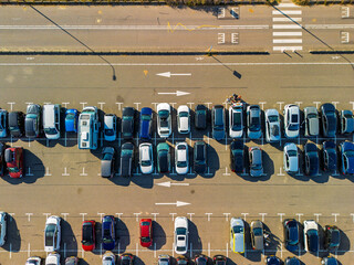 Aerial view of a large, organized parking lot filled with colorful cars. Bright sunlight casts long...