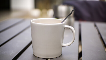 A glass of warm coffee with milk in a white ceramic cup on a gray iron table with a blurred background