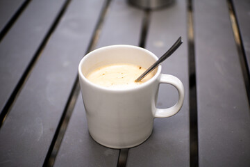 A glass of warm coffee with milk in a white ceramic cup on a gray iron table with a blurred background