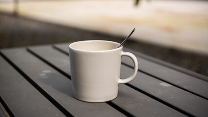 A glass of warm coffee with milk in a white ceramic cup on a gray iron table with a blurred background