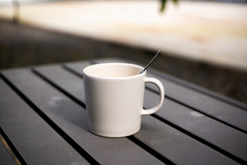 A glass of warm coffee with milk in a white ceramic cup on a gray iron table with a blurred background