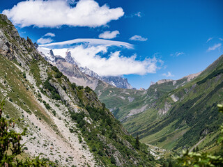 Obraz premium Sunny alpine valley with dramatic peaks and lenticular clouds, French Alps
