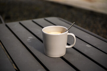 A glass of warm coffee with milk in a white ceramic cup on a gray iron table with a blurred background