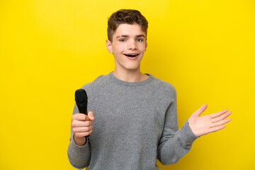 Singer Teenager man picking up a microphone isolated on yellow background with shocked facial...