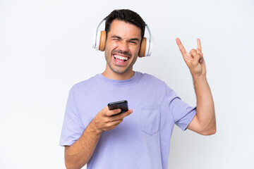 Young handsome man over isolated white background listening music with a mobile making rock gesture