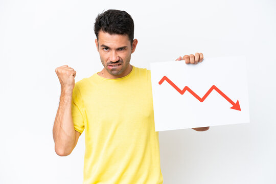 Young handsome man over isolated white background holding a sign with a decreasing statistics arrow symbol and angry